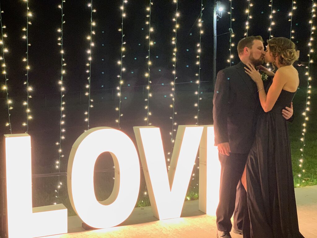 Bride and groom kissing beside illuminated LOVE sign at Grahams Estate