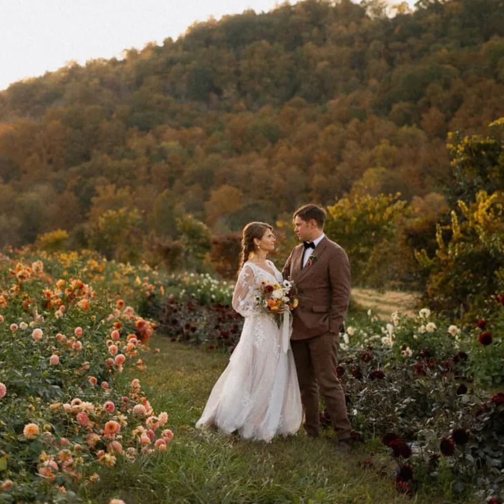 Bride and groom standing in a dahlia field with Asheville mountain scenery behind them.