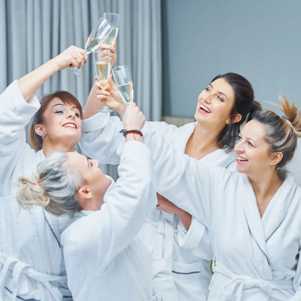 Bridesmaids in white robes toasting champagne on the wedding morning