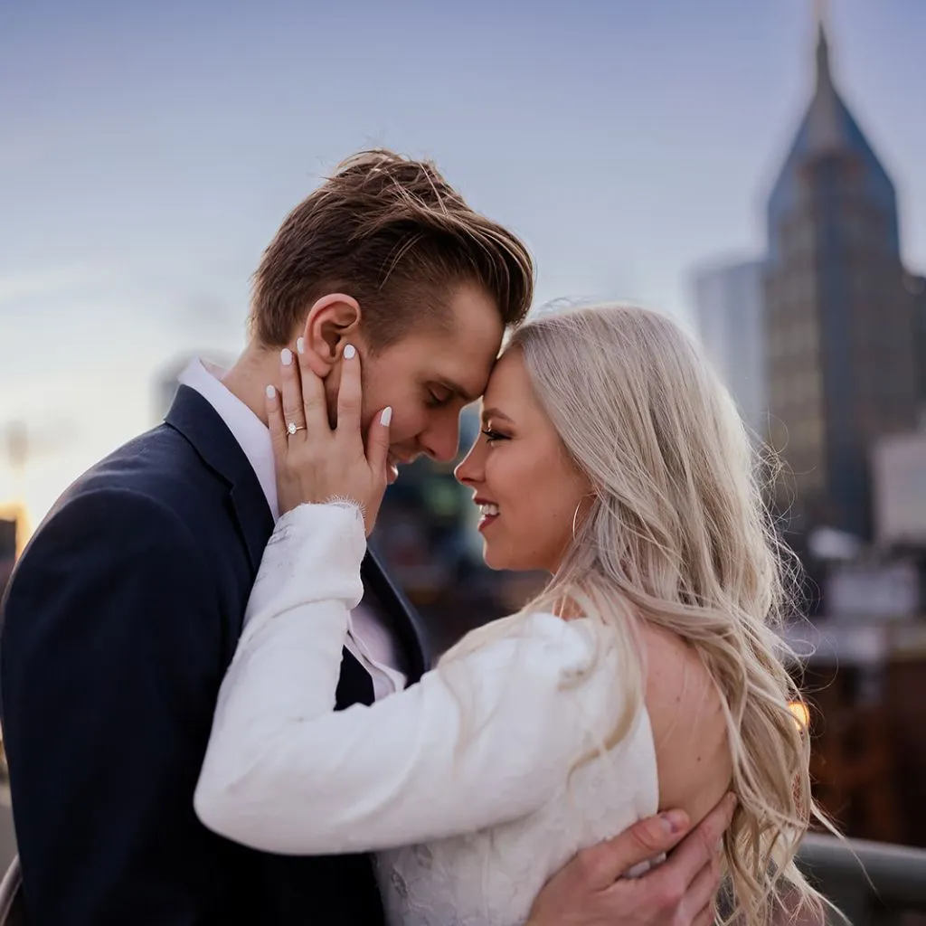 Romantic Nashville engagement photo of a couple kissing with the downtown skyline behind them.