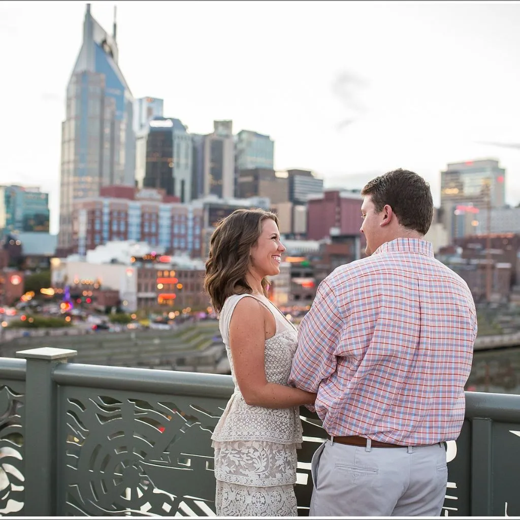 Couple standing on the Nashville pedestrian bridge with the downtown skyline behind them.